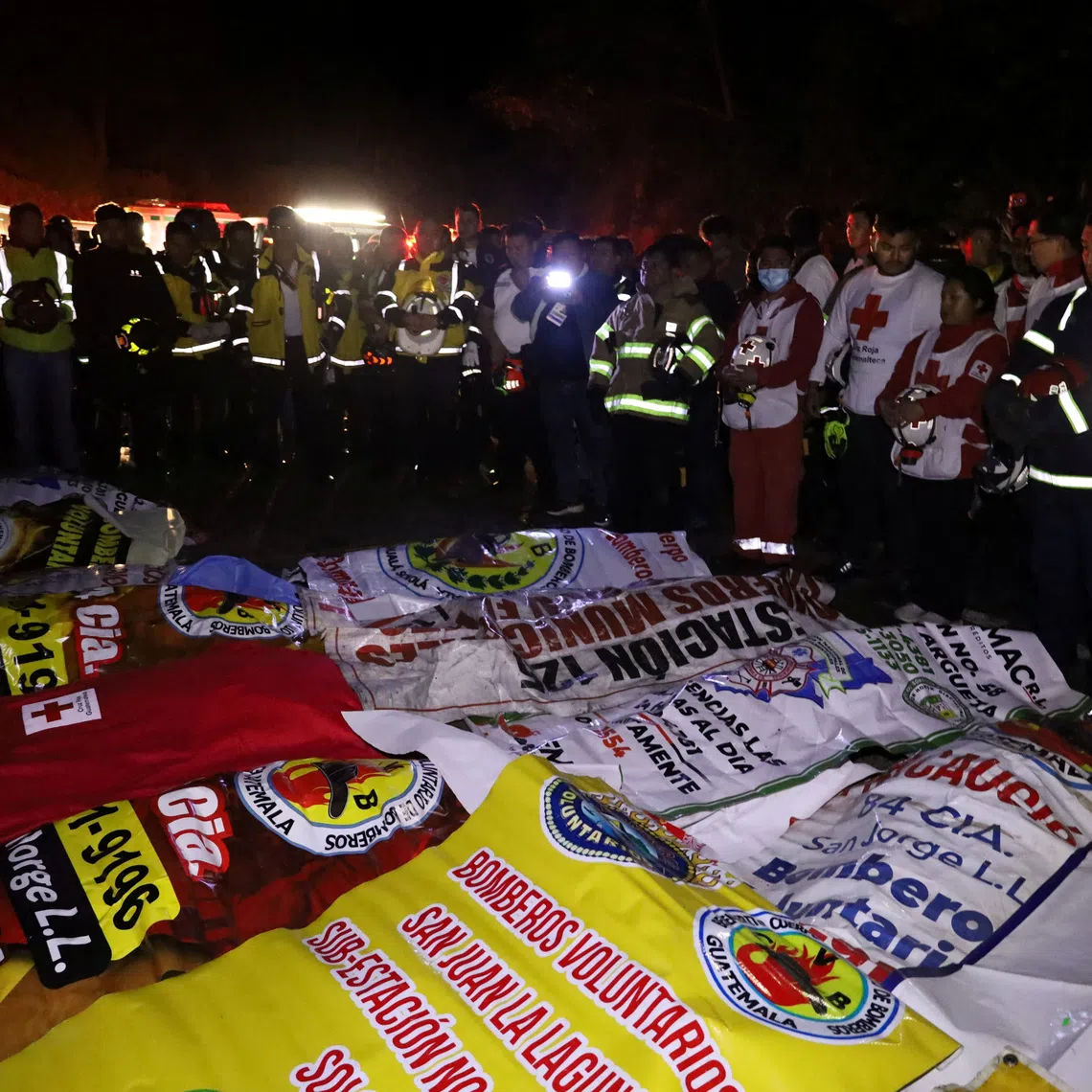 Paramedics and firefighters stand next to the covered bodies of victims after a passenger bus plunged into a ravine, in Totonicapan, Guatemala, December 27, 2025. CVB Volunteer Fire Department/Handout via REUTERS