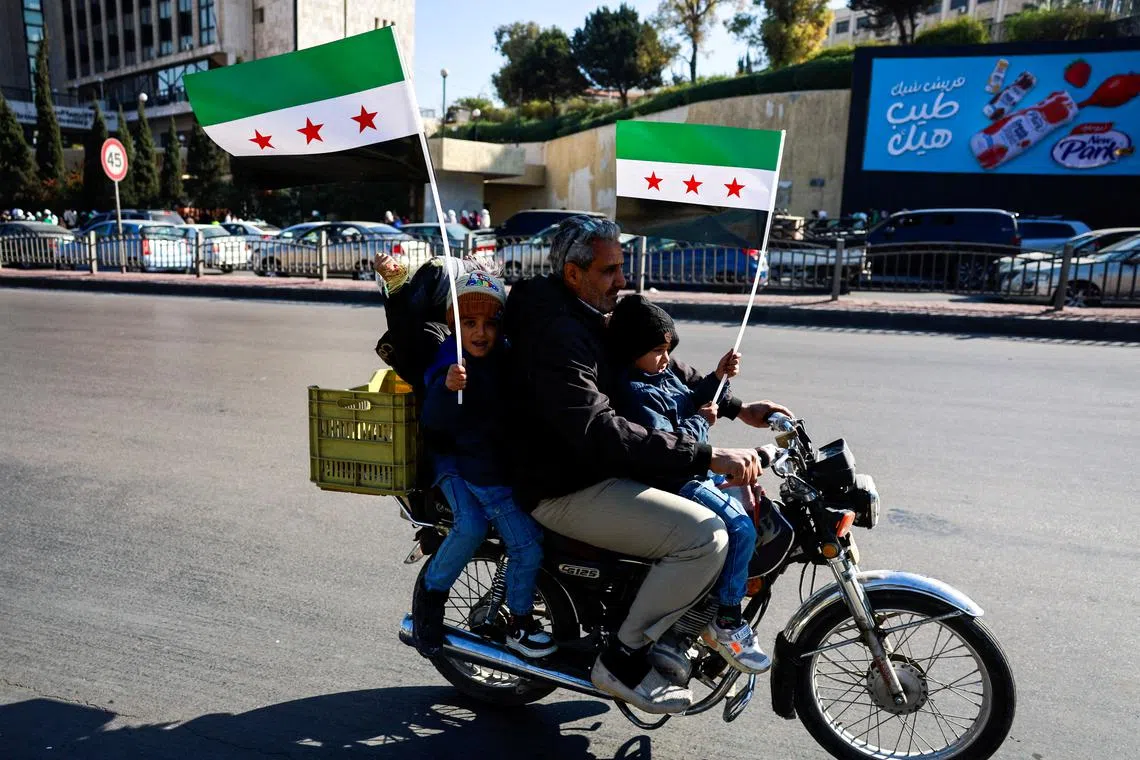A man rides a motorbike with children holding up flags adopted by the new Syrian rulers, after Syria's Bashar al-Assad was ousted, in Damascus, Syria, December 15, 2024. REUTERS/Ammar Awad
