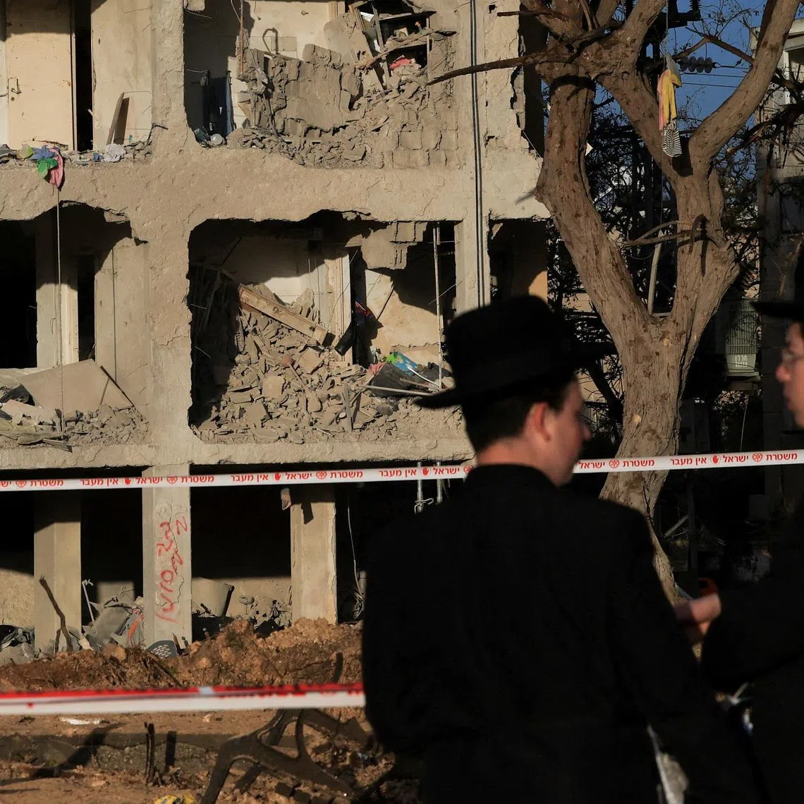 People stand at the scene of damage after Iranian missile barrages struck residential buildings in Arad, amid the U.S.-Israel conflict with Iran, in southern Israel, March 22, 2026. REUTERS/Ronen Zvulun