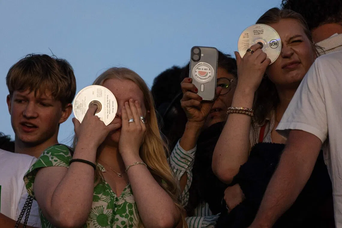 People gather on Skinnarviksberget in Stockholm to watch a partial solar eclipse that covered about 81 percent of the sun at its peak shortly before sunset on August 12, 2026. Millions of people turn their gaze towards the heavens on August 12, 2026 to witness one of nature's greatest spectacles -- a rare total solar eclipse -- as it sweeps over mainland Europe to briefly turn day into night. (Photo by Jonathan NACKSTRAND / AFP)