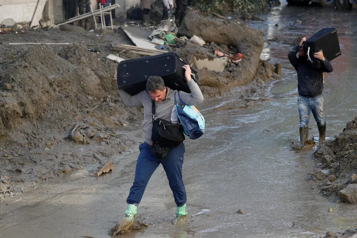 Men carry baggage as they walk on a street covered in mud and debris, following a landslide on the Italian holiday island of Ischia, Italy, Nov 27, 2022. 