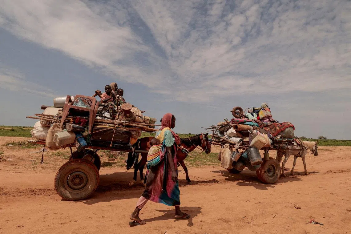 FILE PHOTO: A Sudanese woman, who fled the conflict in Murnei in Sudan's Darfur region, walks beside carts carrying her family belongings upon crossing the border between Sudan and Chad in Adre, Chad August 2, 2023. REUTERS/Zohra Bensemra/File Photo