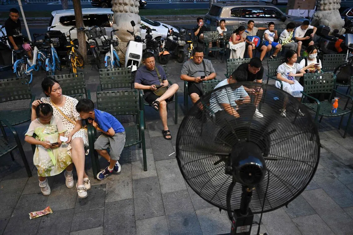 People sit in front of a fan as they wait for seats at a restaurant during a heat wave in Beijing on July 19.
