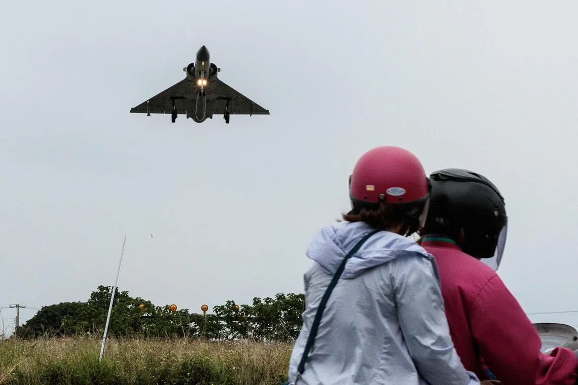 Two people ride a motorcycle as a Taiwanese Air Force Mirage 2000 fighter jet approaches for landing at an air force base in Hsinchu in northern Taiwan on May 23, 2024. 