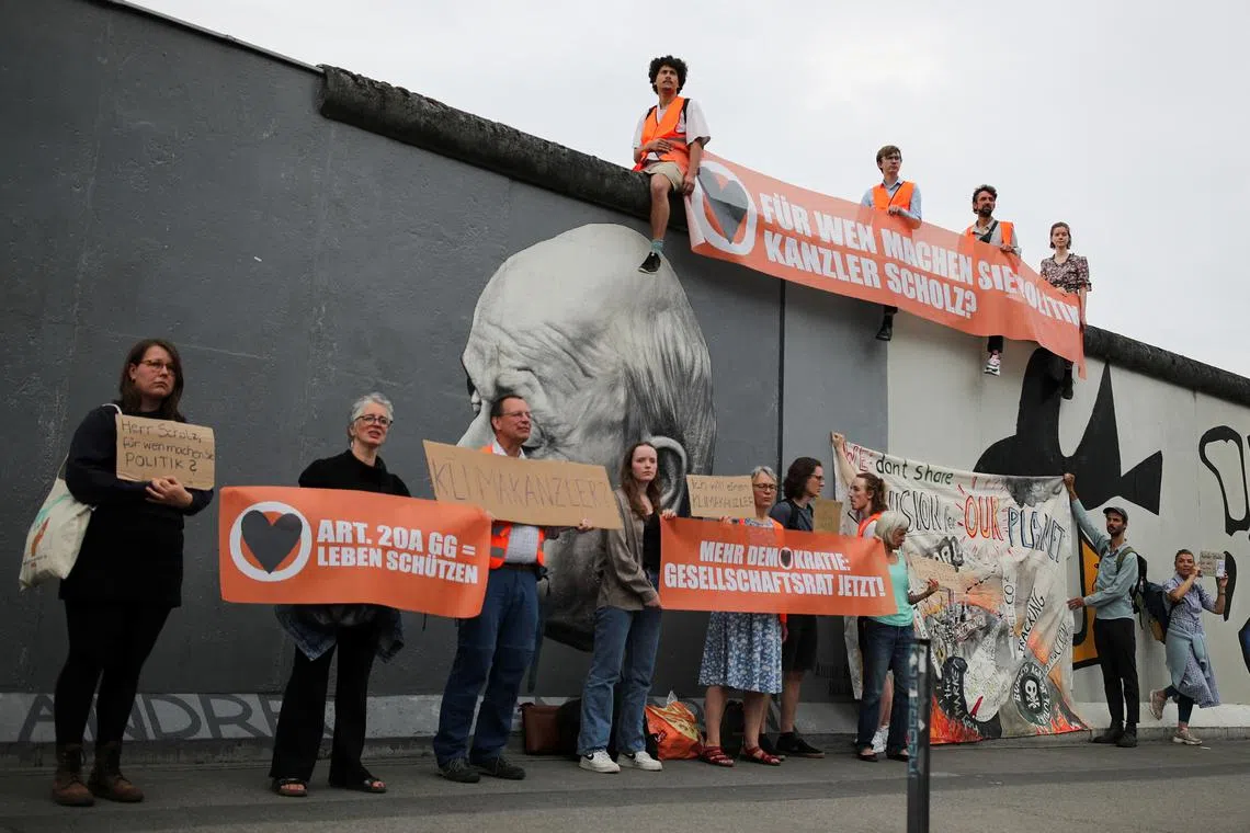 Climate Change activists of Letzte Generation sit on the original remnants of the Berlin Wall during a protest.