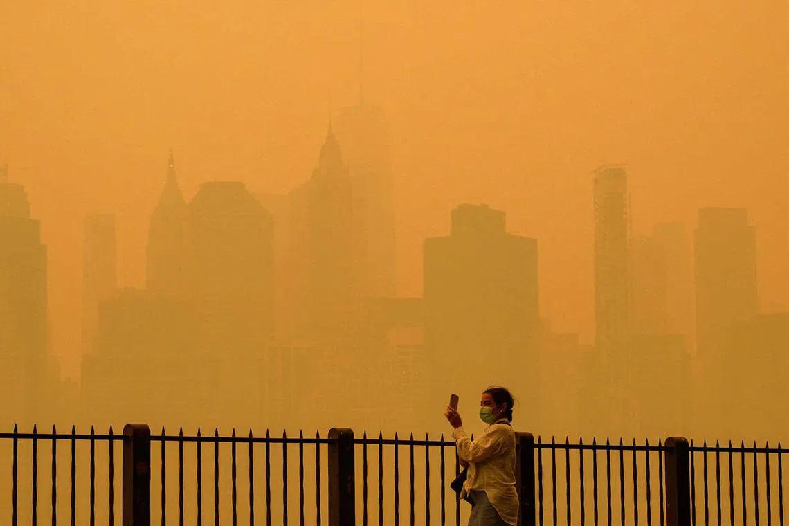 A person wearing a face mask takes photos of the skyline as smoke from wildfires in Canada cause hazy conditions in New York City on June 7. 