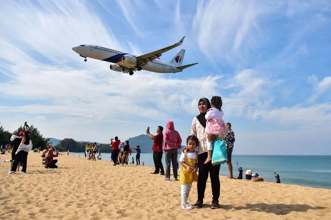 Tourists posing for pictures on Mai Khao Beach as a plane lands at Phuket International Airport in Phuket. 