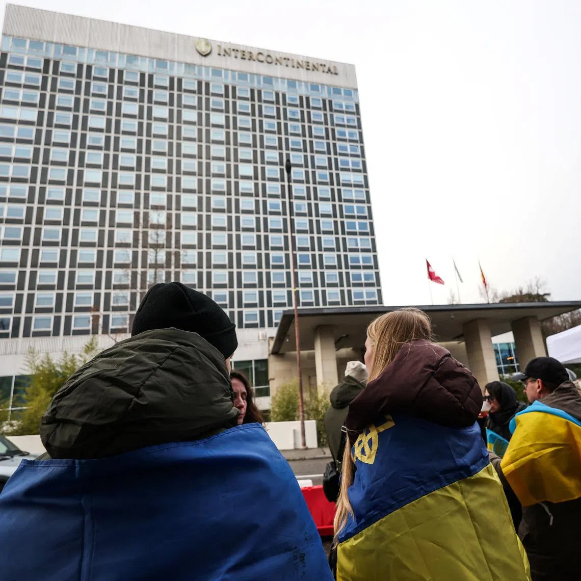 People wrapped in Ukrainian flags stand outside the InterContinental hotel, on the day of US-mediated peace talks between Russia and Ukraine, in Geneva on Feb 17.