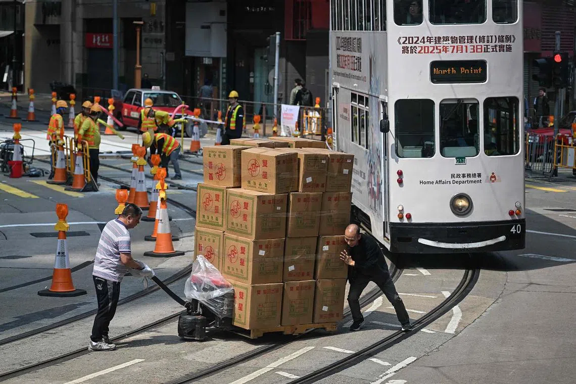 TOPSHOT - Two men push a pallet of goods over tram tracks in Hong Kong on April 2, 2025. Asian markets edged up as nervous investors brace for US President Donald Trump's wave of tariffs later in the day, though speculation about what he has in store is stoking uncertainty on trading floors. (Photo by Peter PARKS / AFP)
