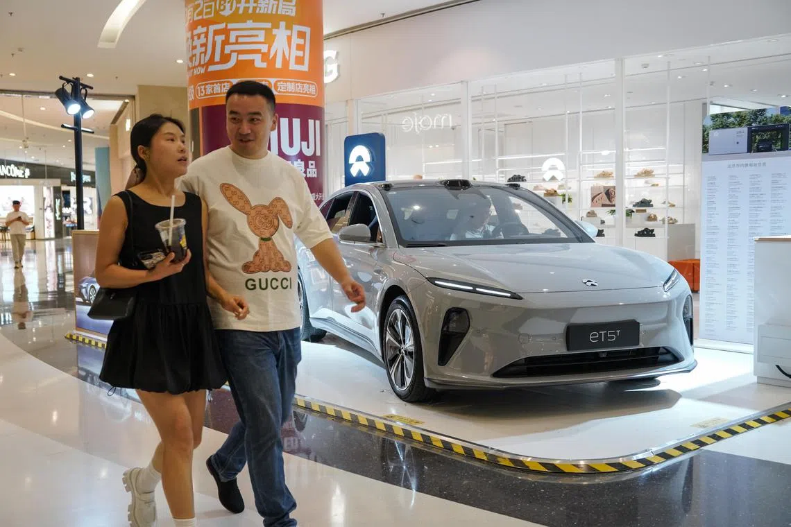 People walk beside a NIO ET5 electric car on display in a shopping mall in Beijing, China on June 13, 2024. 
