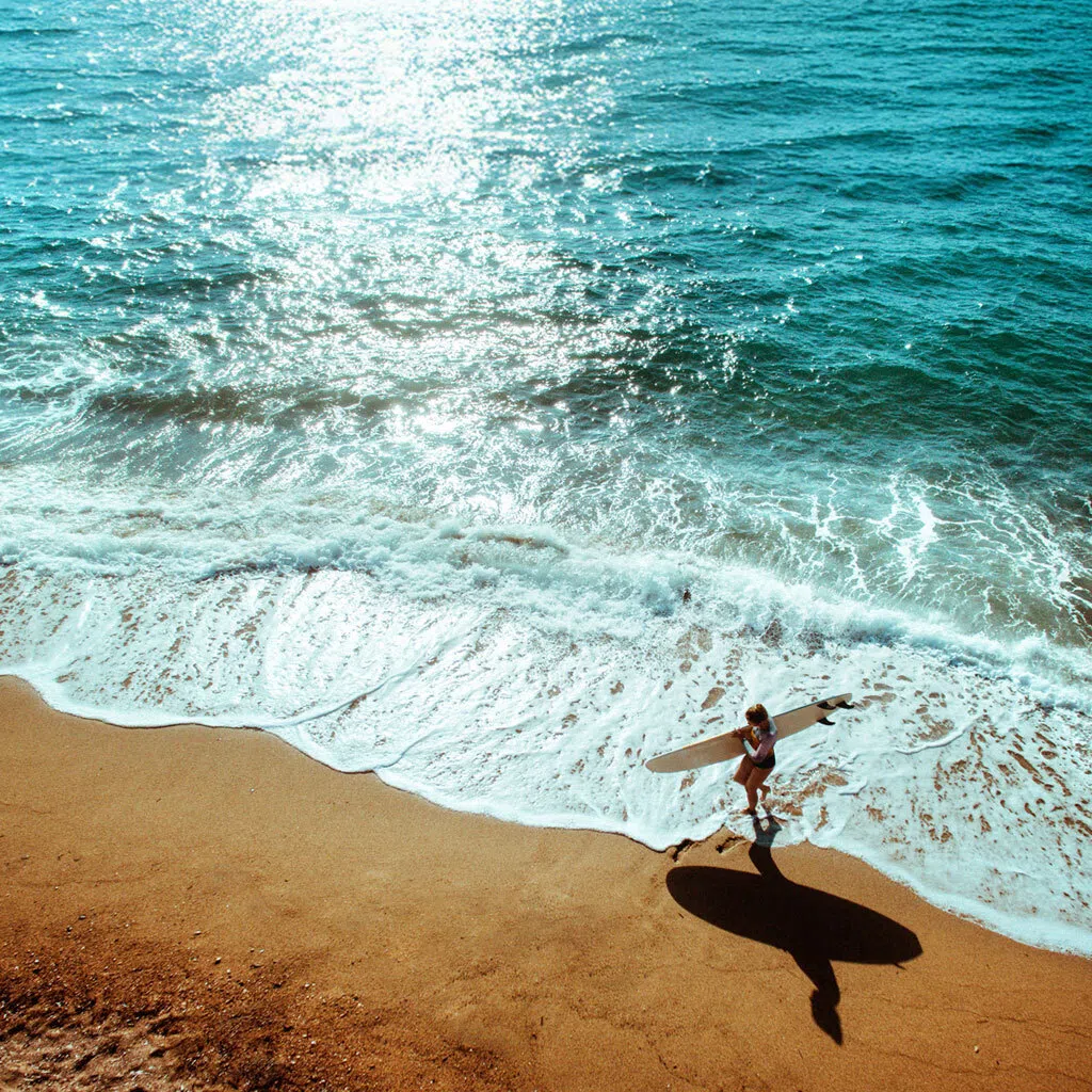 Person walking along a beach holding a surfing board