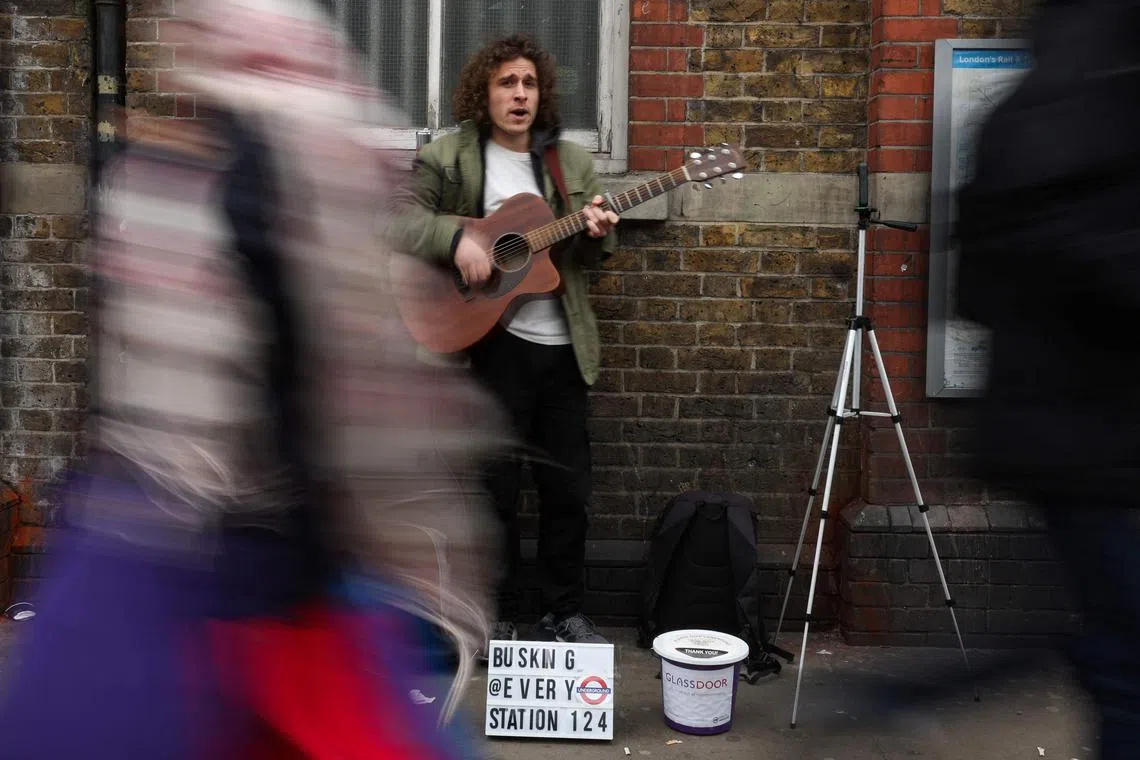 Australia's Dan Tredget plays his guitar while busking in the street outside of a metro station in London on March 19, 2024. He is aiming to become the first person to busk at every London Underground station. 