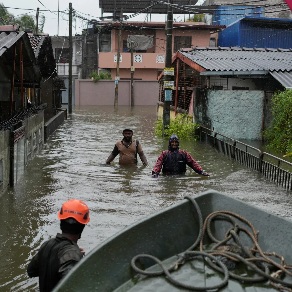 People walk along a flooded street, following heavy rainfall in Wellampitiya, Sri Lanka, on Nov 28.