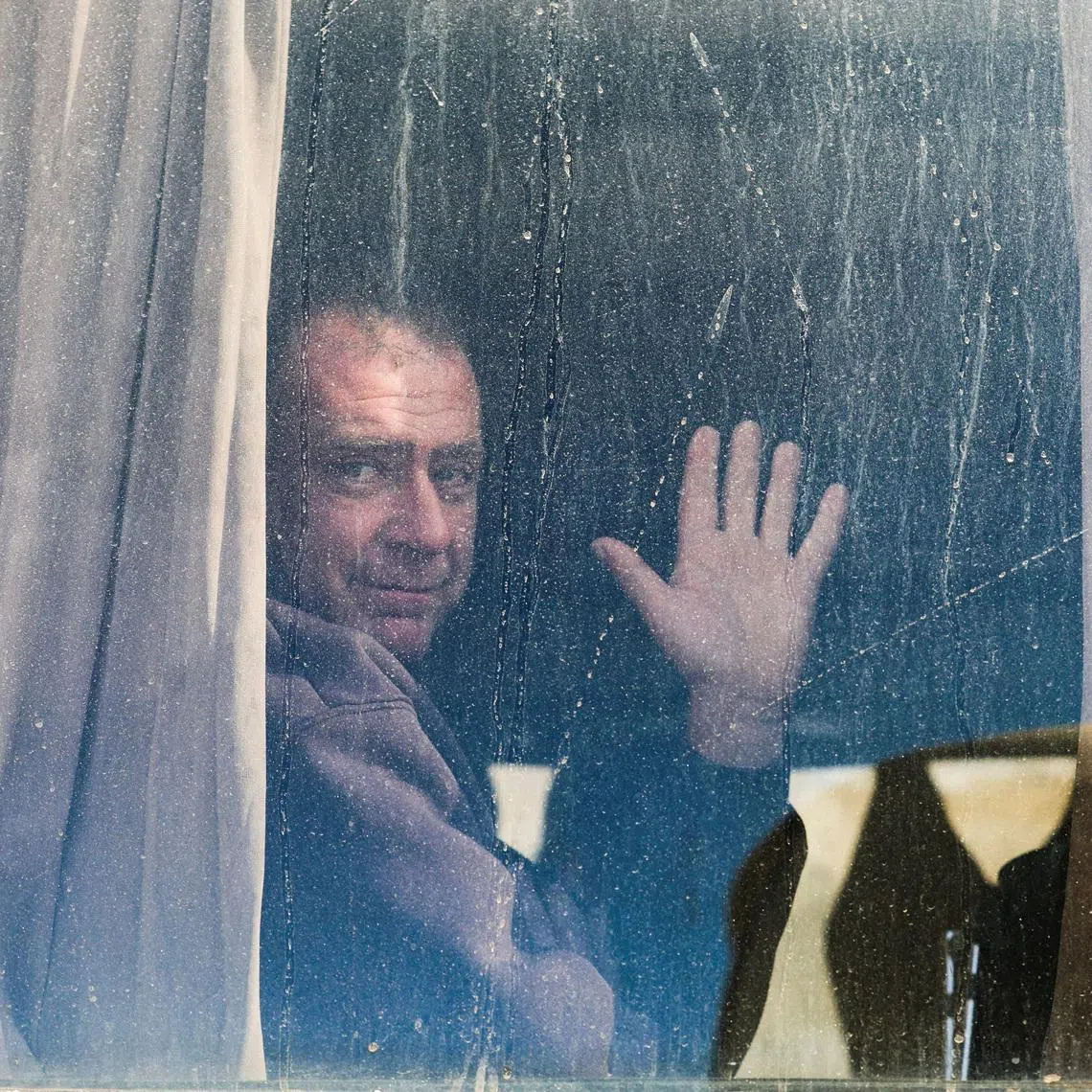 A Palestinian man waves from a window as war-wounded people and patients, accompanied by relatives, get ready to leave Gaza for treatment abroad through the Rafah border crossing between Gaza and Egypt, after it was opened by Israel on Monday for a limited number of people, in Khan Younis in the southern Gaza Strip, February 3, 2026. 
