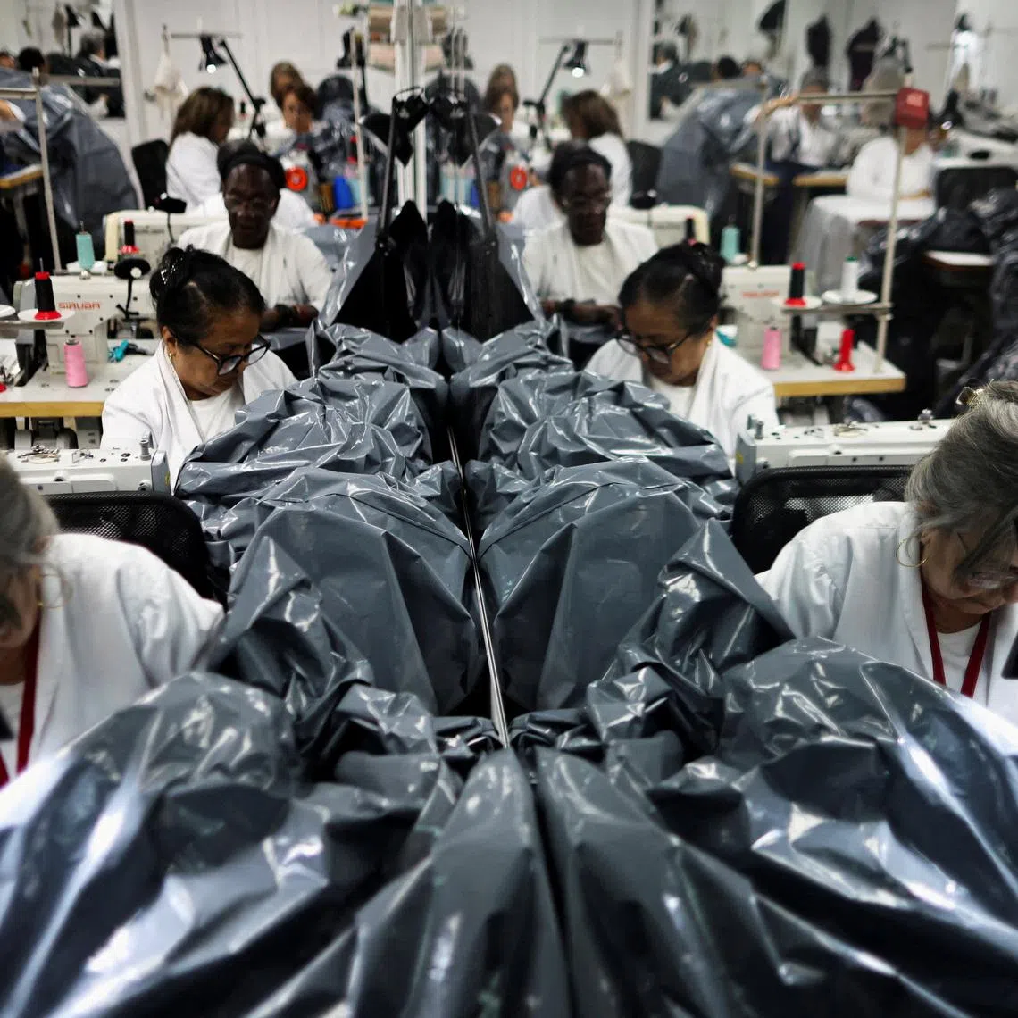 Workers make body bags, as they are reflected in a mirror, at a workshop where they are made for donation to rescue teams assisting in the recovery of victims following the June 24 earthquakes, in Maracay, Venezuela, July 7, 2026. REUTERS/Adriano Machado