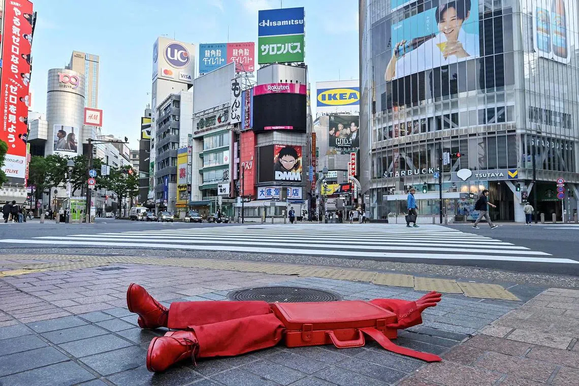 An art installation by French street artist James Colomina, called The Briefcase, is pictured on the pavement at Shibuya Crossing in the Shibuya district of central Tokyo on May 20, 2025. The display shows a red briefcase - a symbol of work and conformity - with arms, legs and a tie poking out on the ground to illustrate a salaryman who has lost his identity, swallowed by his daily routine.