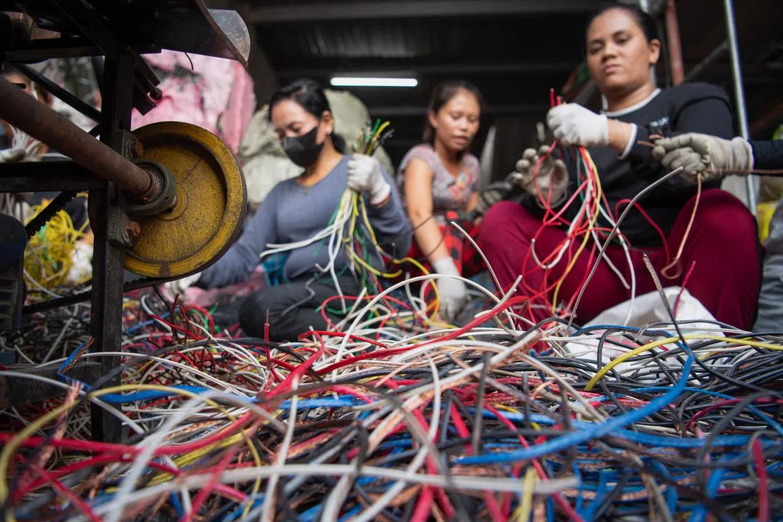 TOPSHOT - This photo taken on June 26, 2025 shows workers removing copper from industrial wiring inside a recycling shop in Manila. Stripping scrapped laptops and air conditioners for metal frequently involves burning away rubber wire casings, releasing a toxic brew of chemicals including lead, mercury and cadmium into the air. The World Health Organization last year said exposure to e-waste chemicals can lead to incidents of asthma and reduced lung function in children, while pregnant women are at higher risk for stillbirths and premature delivery. (Photo by Ted ALJIBE / AFP) / To go with AFP story Philippines-health-environment-recycling, FOCUS by Pam Castro