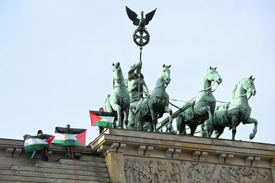 Pro-Palestinian protesters waving Palestinian flags on top of Brandenburg Gate in Berlin, after using a rented cherry-picker truck to unfurl a banner, on Nov 13.