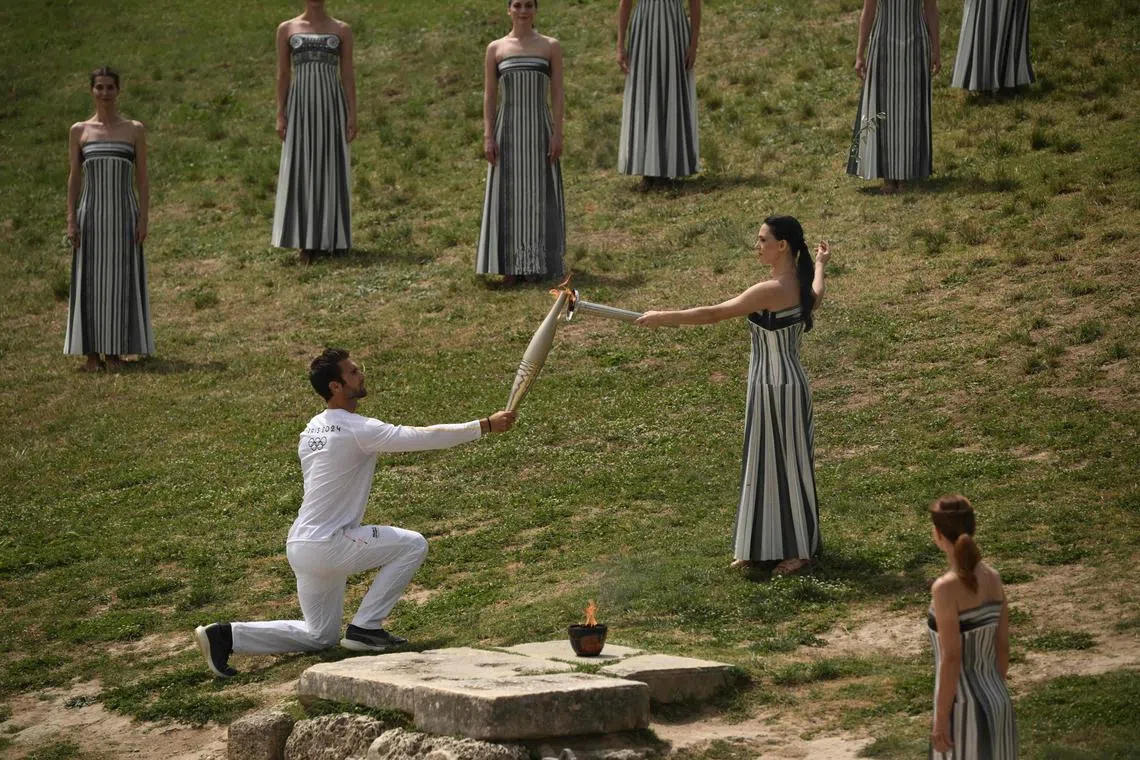 First torch bearer Stephanos Ntouskos receiving the flame from Greek actress Mary Mina, playing the role of the High Priestess, as he starts his run with the Olympic torch following the flame lighting ceremony for the Paris 2024 Olympics Games.