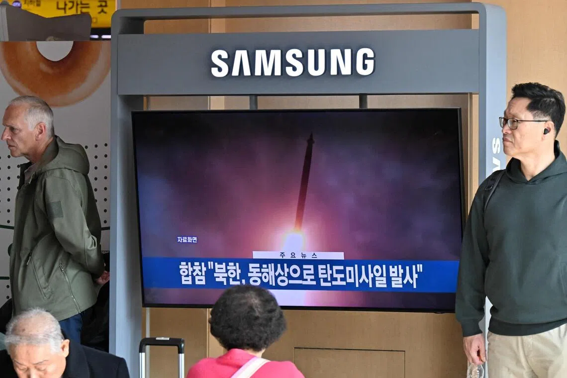 People stand next to a television showing a news broadcast with file footage of a North Korean missile test, at a railway station in Seoul on Nov 7, 2025. 