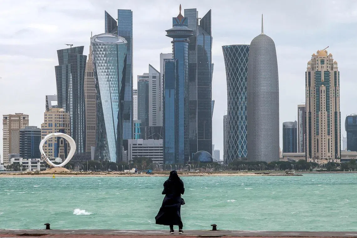 A woman standing by the waterfront at the Doha corniche facing high-rise buildings in the West Bay district, in Doha, Qatar, on April 16, 2024