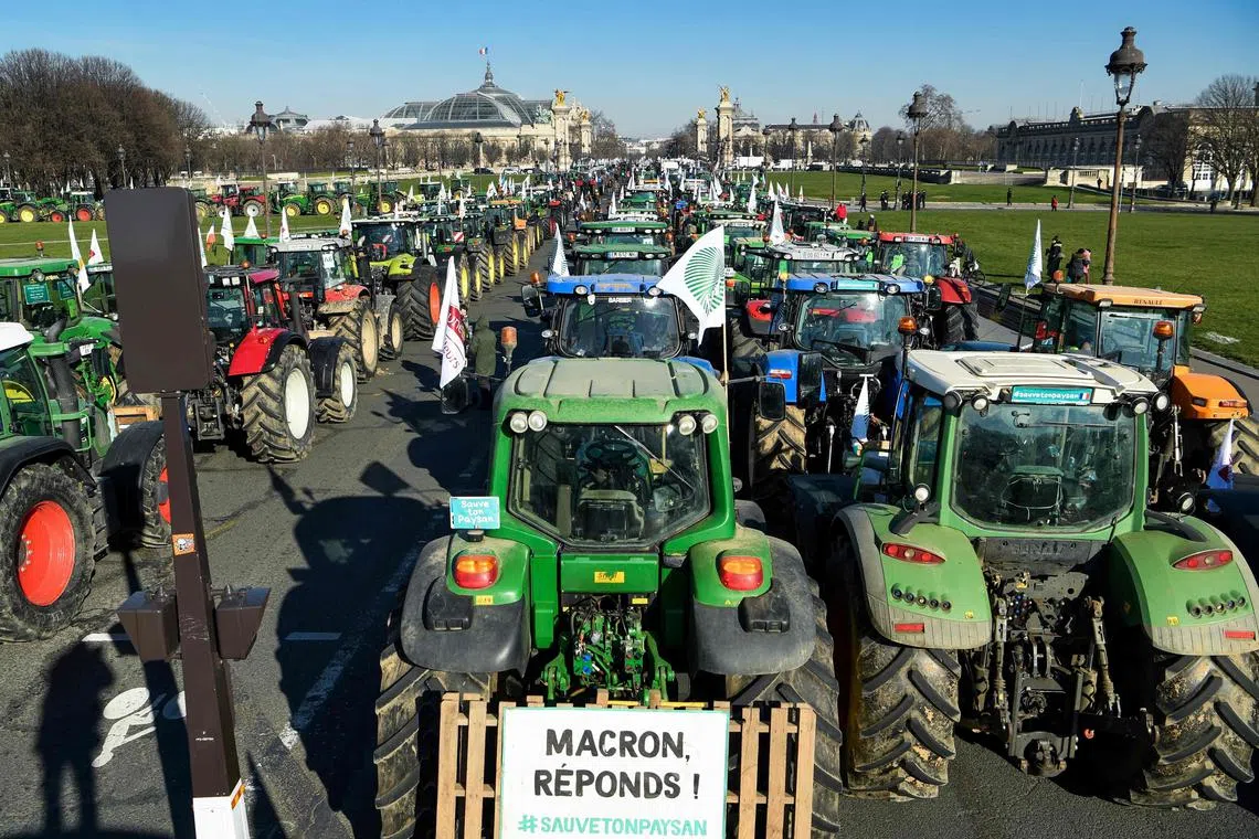 This photograph shows a sign reading "Macron, anwers !" as farmers stand next to tractors at the Esplanades des Invalides during a demonstration organised by unions including FNSEA (National Federation of Farmers Union), against "obligations" in agriculture, in particular restrictions on the use of pesticides, in Paris, on Feb 8 2023. 