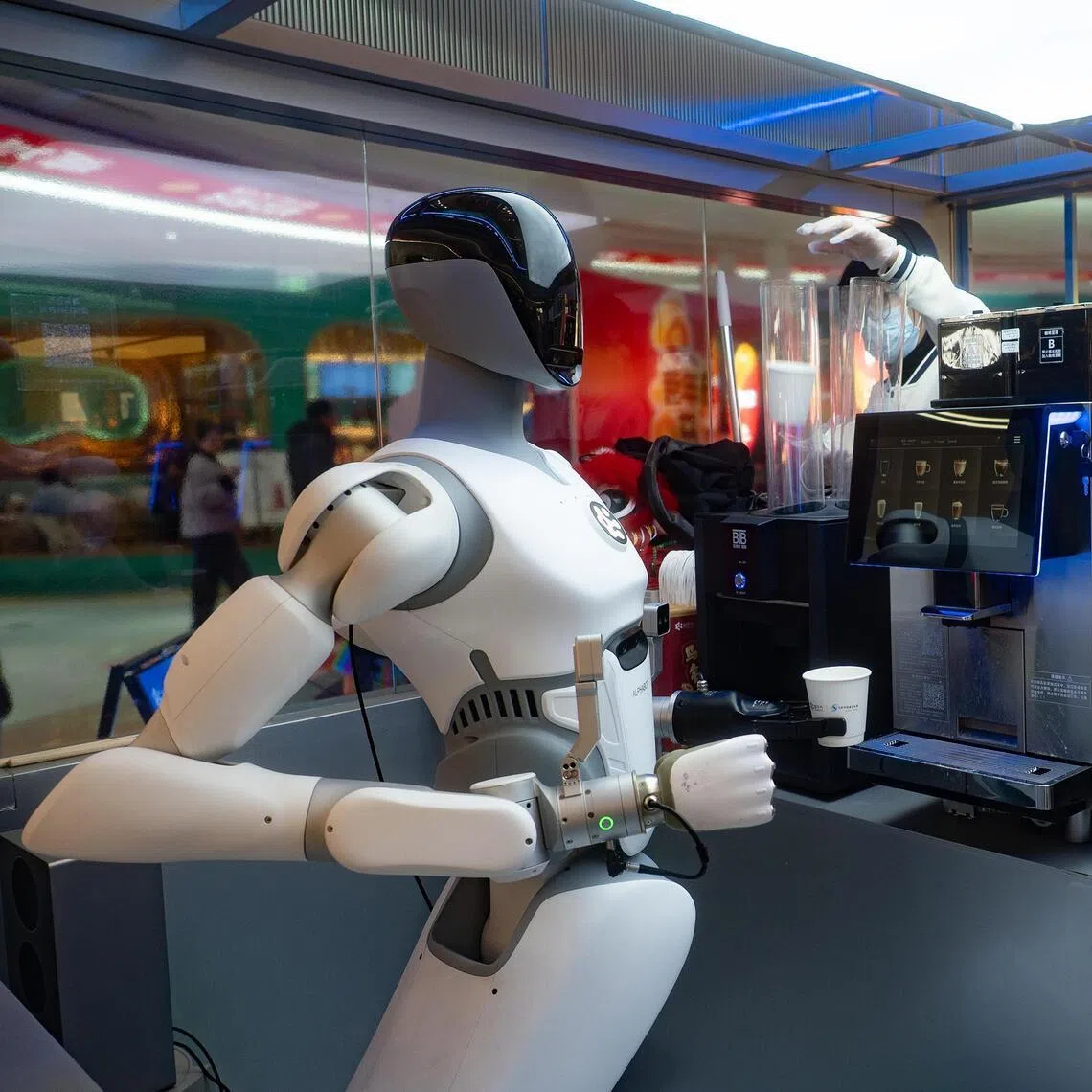 jyrobot - A humanoid robot by Chinese company Zhipingfang serves coffee made by a coffee machine, while a human shop assistant loads cups for use. ST PHOTO: LIM MIN ZHANG
