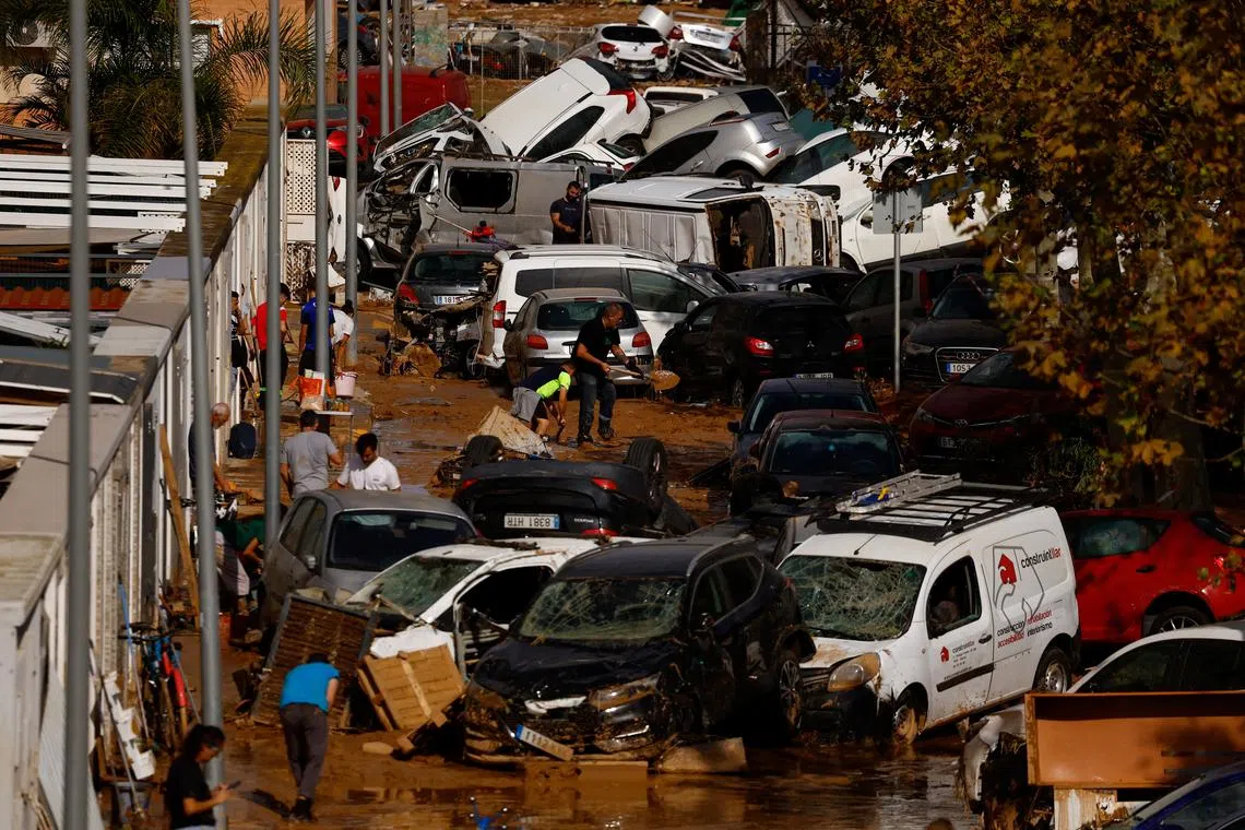 People clean up a mud-covered street next to piled up cars after heavy rains in Alfafar, in Valencia, Spain, November 1, 2024. REUTERS/Susana Vera