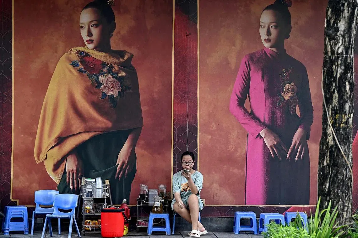 A girl using a mobile phone at a tea stall in front of clothing advertisements in Hanoi on Aug 12, 2024.