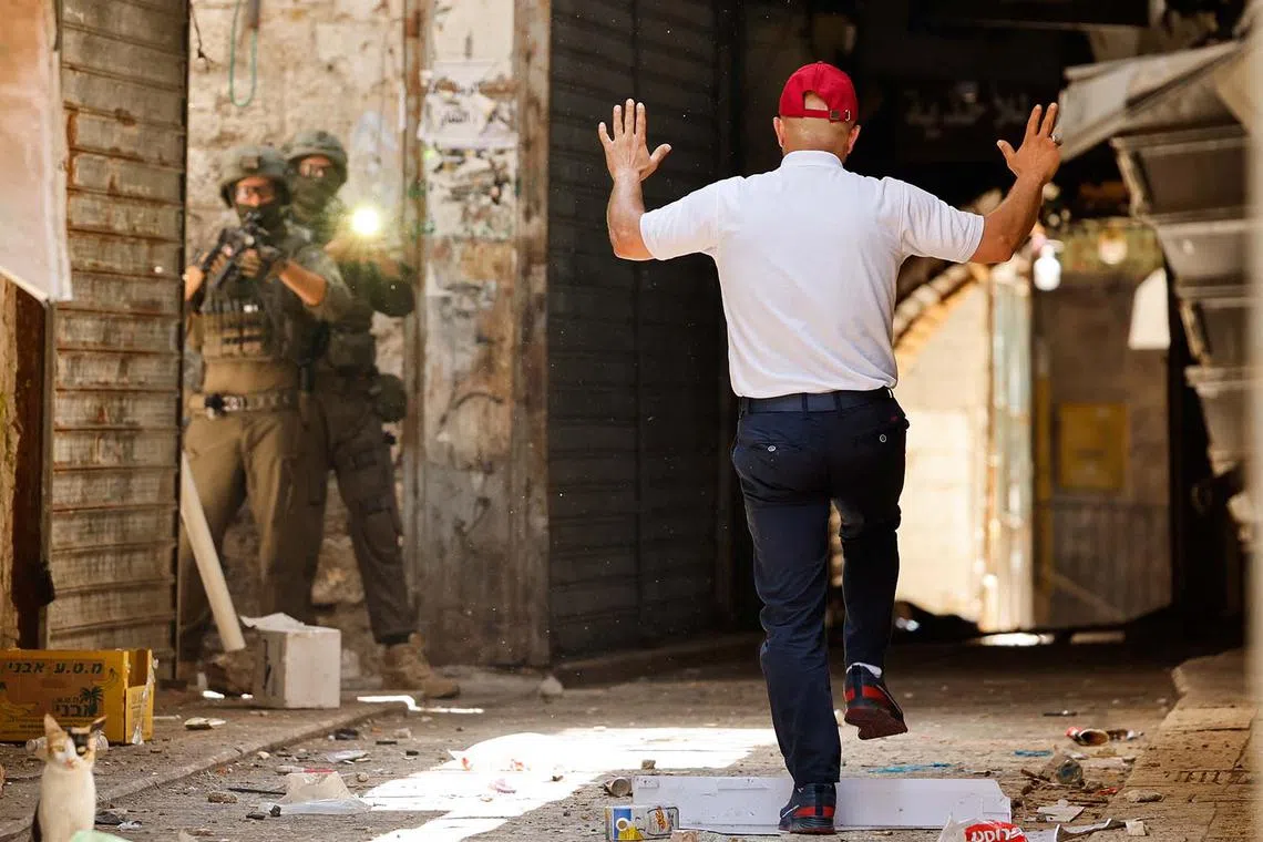 A Palestinian man raising his hands as Israeli soldiers aim their weapons during a raid in Nablus, the Israeli-occupied West Bank, June 10, 2025. 