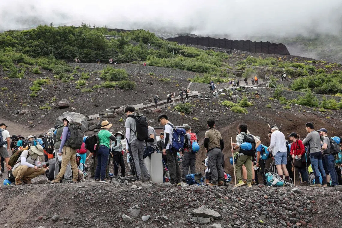 This photo taken on August 31, 2023 shows visitors climbing the slopes of Mount Fuji, Japan's highest peak at 3,776 meters (12,388 feet). With its millions of visitors every year and the buses, supply trucks, noodle shops and fridge magnets, Mount Fuji is no longer the peaceful, nature-filled pilgrimage site it once was. (Photo by Mathias CENA / AFP) / TO GO WITH Japan-leisure-environment,FOCUS by Mathias CENA