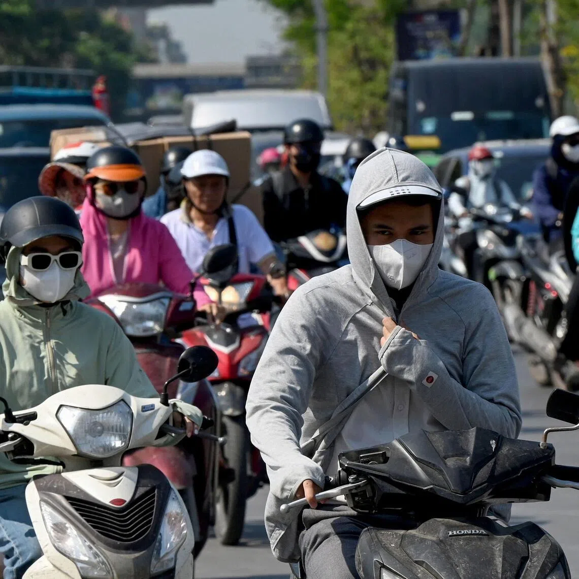 Motorists ride scooters and motorbikes along a street on a hot day in Hanoi on May 27. 
