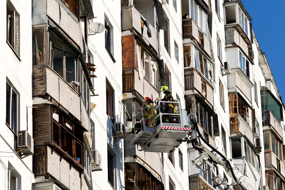 Emergency workers remove lose debris after a nearby impact blew out the windows of an apartment building during Russian missile and drone strikes in Kyiv.