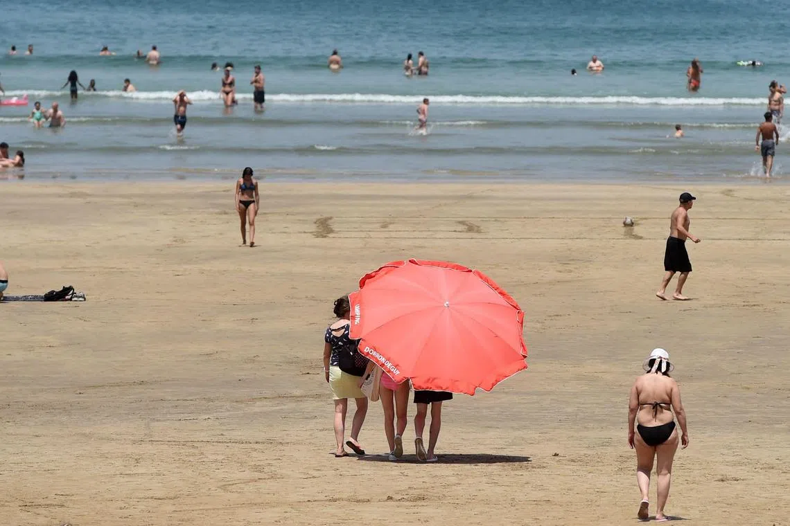 Beachgoers shelter in the shade of an umbrella as they walk on the sands in Hendaye, south-western France on June 18, 2022.