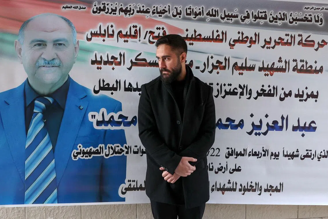Palestinian nurse Elias al-Ashqar stands by a billboard bearing an obituary for his father, Abdel Aziz, on Feb 24, 2023.
