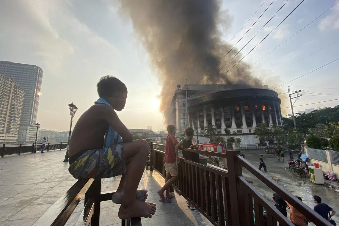 People look on as flames and smoke rise from the burning Philippine Central Post Office building in Manila, Philippines, May 22, 2023. 