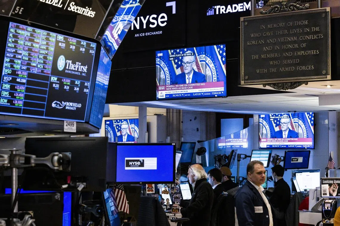 Traders work on the floor of the New York Stock Exchange, as US Federal Reserve chairman Jerome Powell gives a press briefing on TV screens.