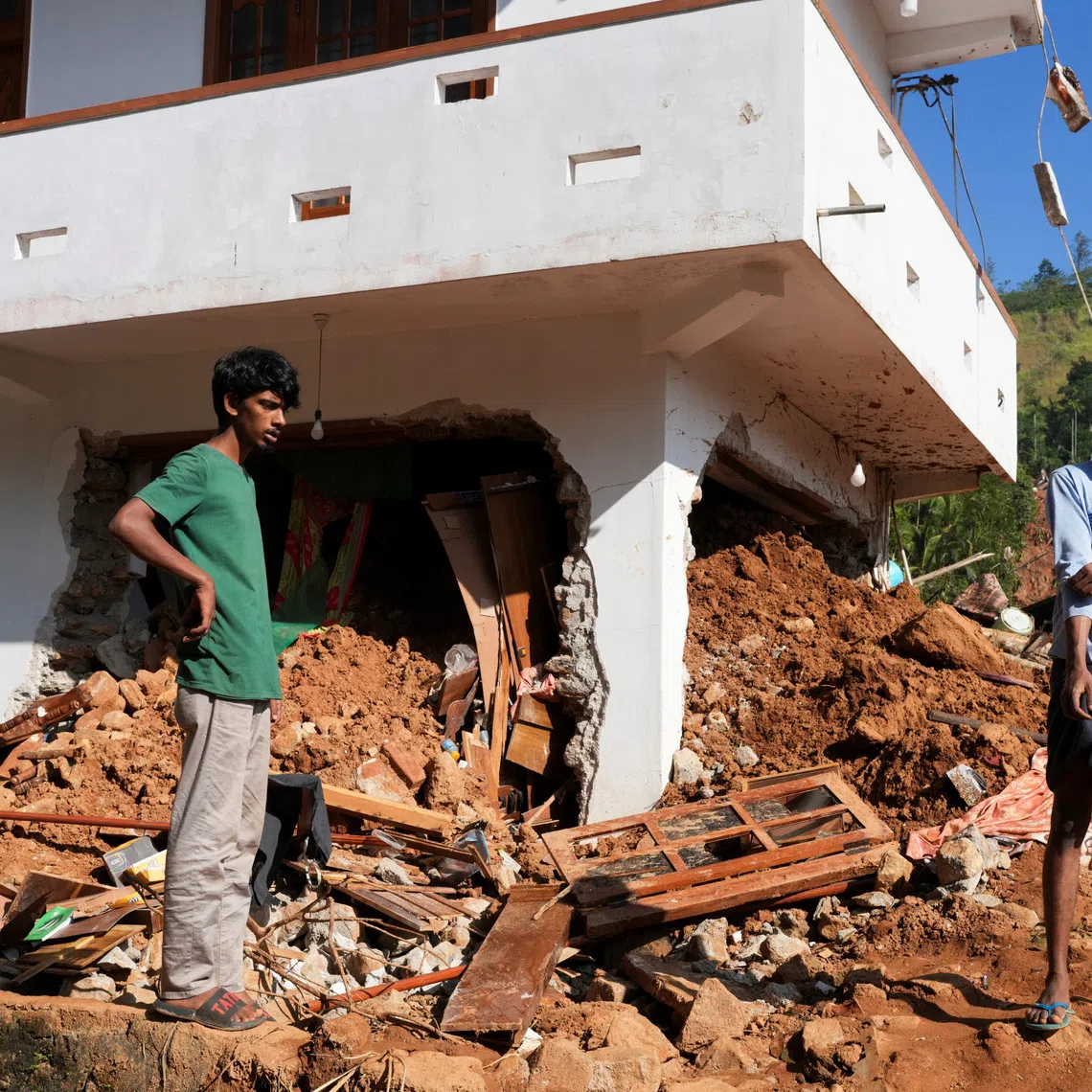 People stand next to debris near a damaged house after landslides caused by heavy rainfall following Cyclone Ditwah in Kandy, Sri Lanka, December 2, 2025. REUTERS/Thilina Kaluthotage