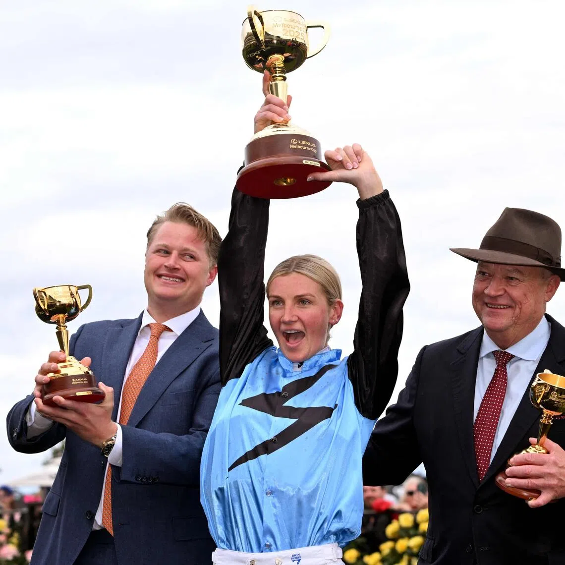 Half Yours Australian jockey Jamie Melham (C) holds the trophy with trainers Calvin McEvoy (L) and Tony McEvoy (R) after her victory in the Melbourne Cup horse race at the Flemington Racecourse in Melbourne on November 4, 2025. Melham became only the second woman jockey to win the Aus$10 million (US$6.5 million) Melbourne Cup on November 4, steering Half Yours to victory in Australia's "race that stops a nation". (Photo by William WEST / AFP) / -- IMAGE RESTRICTED TO EDITORIAL USE - STRICTLY NO COMMERCIAL USE --