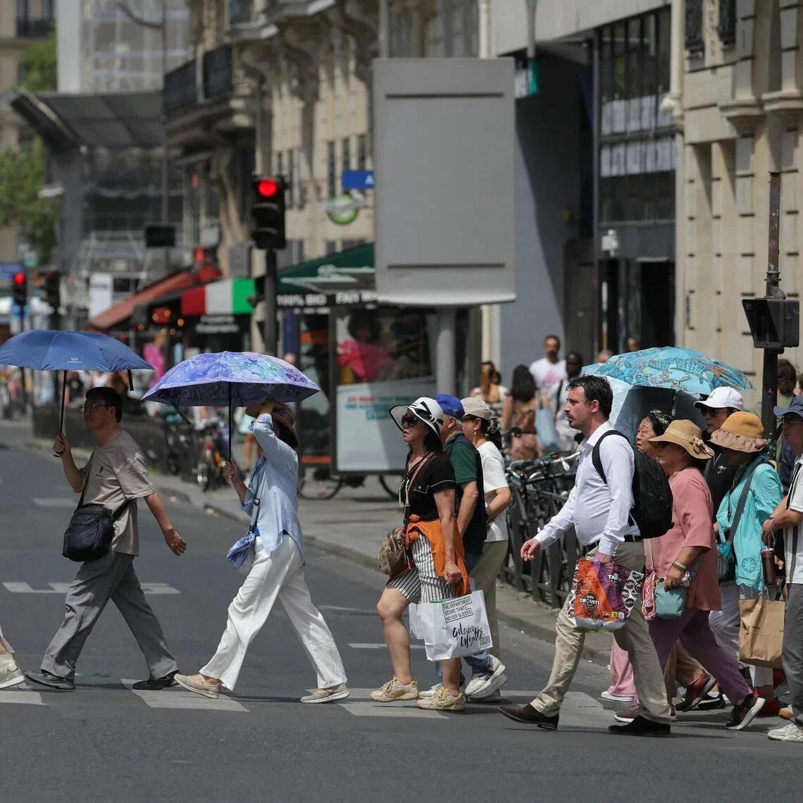 Tourists protecting themselves from the sun under umbrellas while crossing a street in Paris on June 23.