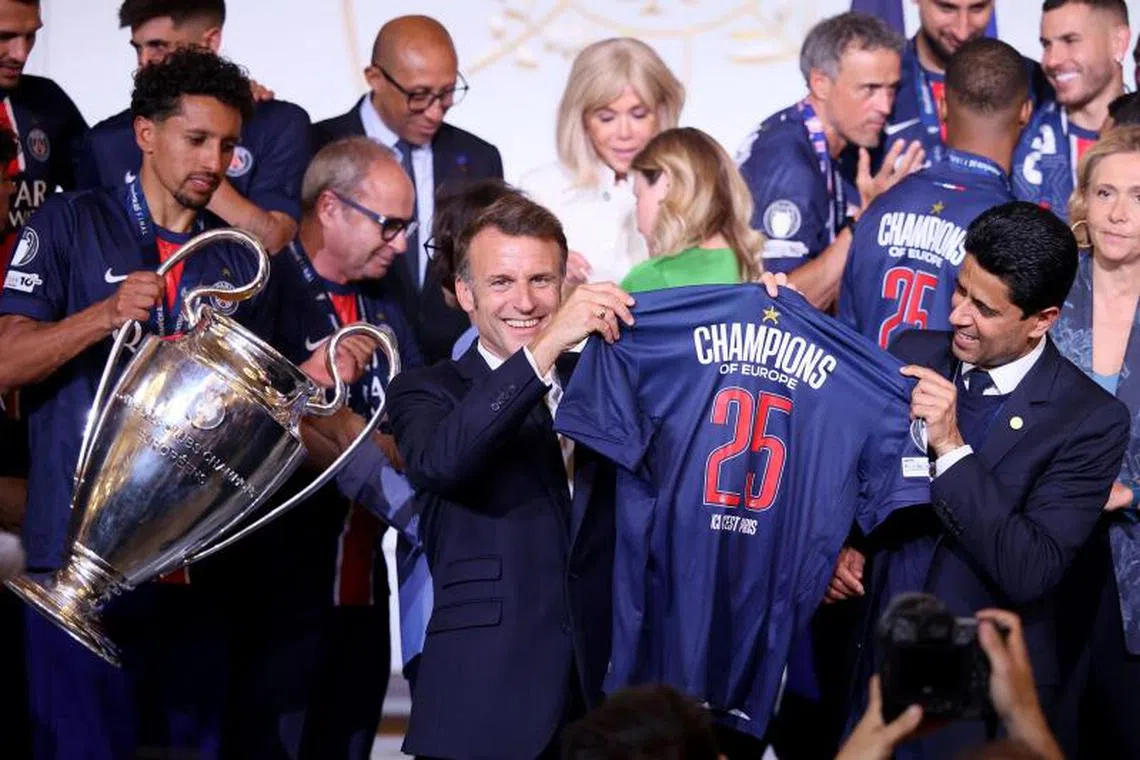 France's President Emmanuel Macron (C) and Paris Saint Germain's Qatari president Nasser al-Khelaifi (R) hold a jersey as Paris Saint-Germain's Brazilian defender #05 Marquinhos (L) holds the trophy during the reception at the Elysee presidential palace in Paris on June 1, 2025, a day after PSG won the 2025 UEFA Champions League final football match against Inter Milan in Munich. (Photo by Thomas PADILLA / POOL / AFP)