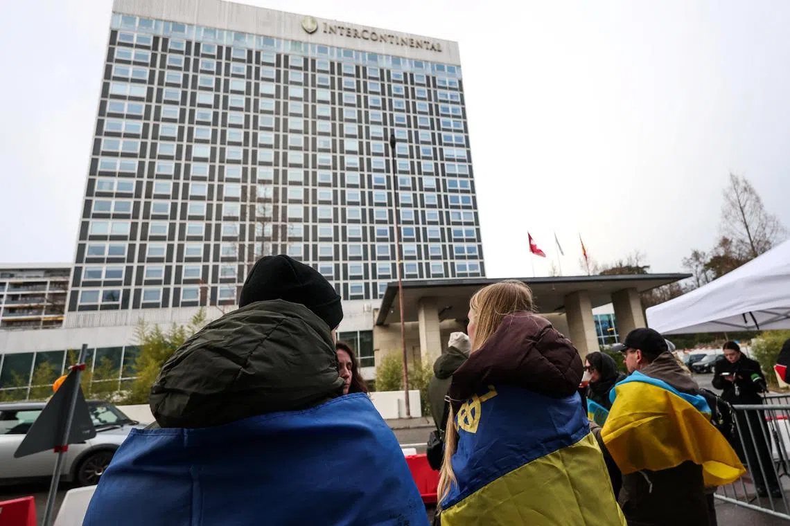 People wrapped in Ukrainian flags stand outside the InterContinental hotel, on the day of US-mediated peace talks between Russia and Ukraine, in Geneva on Feb 17.