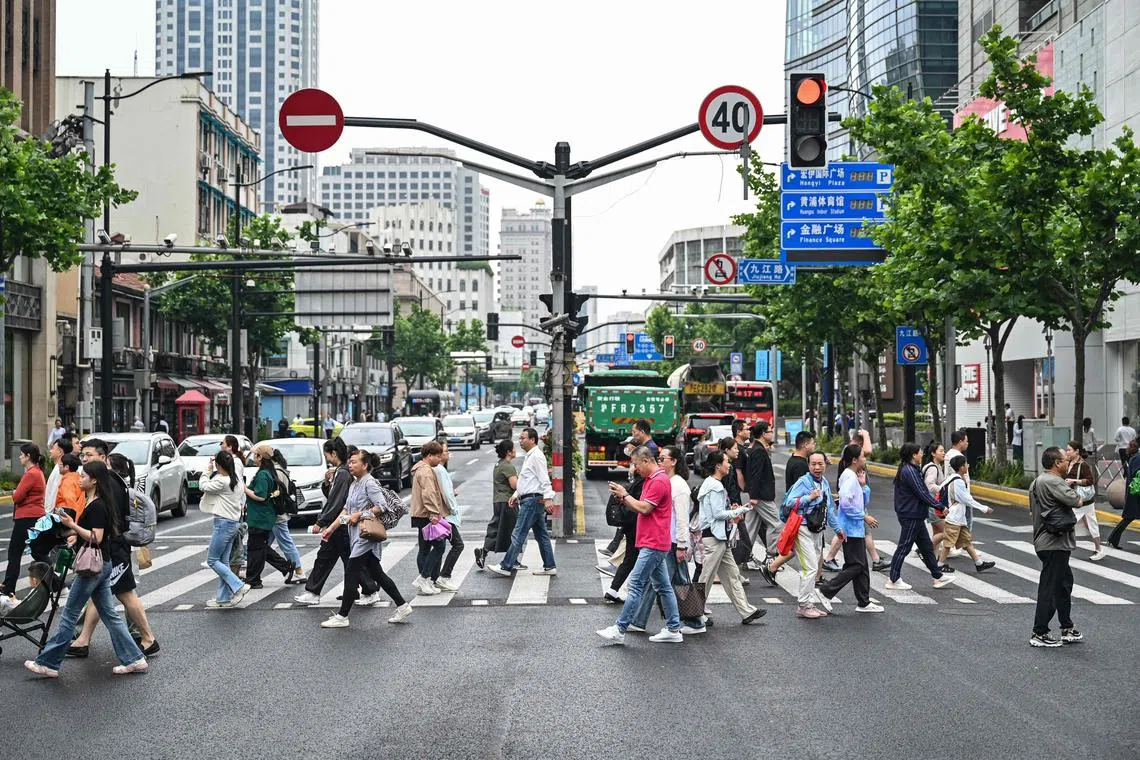 People cross a street in the Huangpu district in Shanghai on June 6, 2024. (Photo by Hector RETAMAL / AFP)