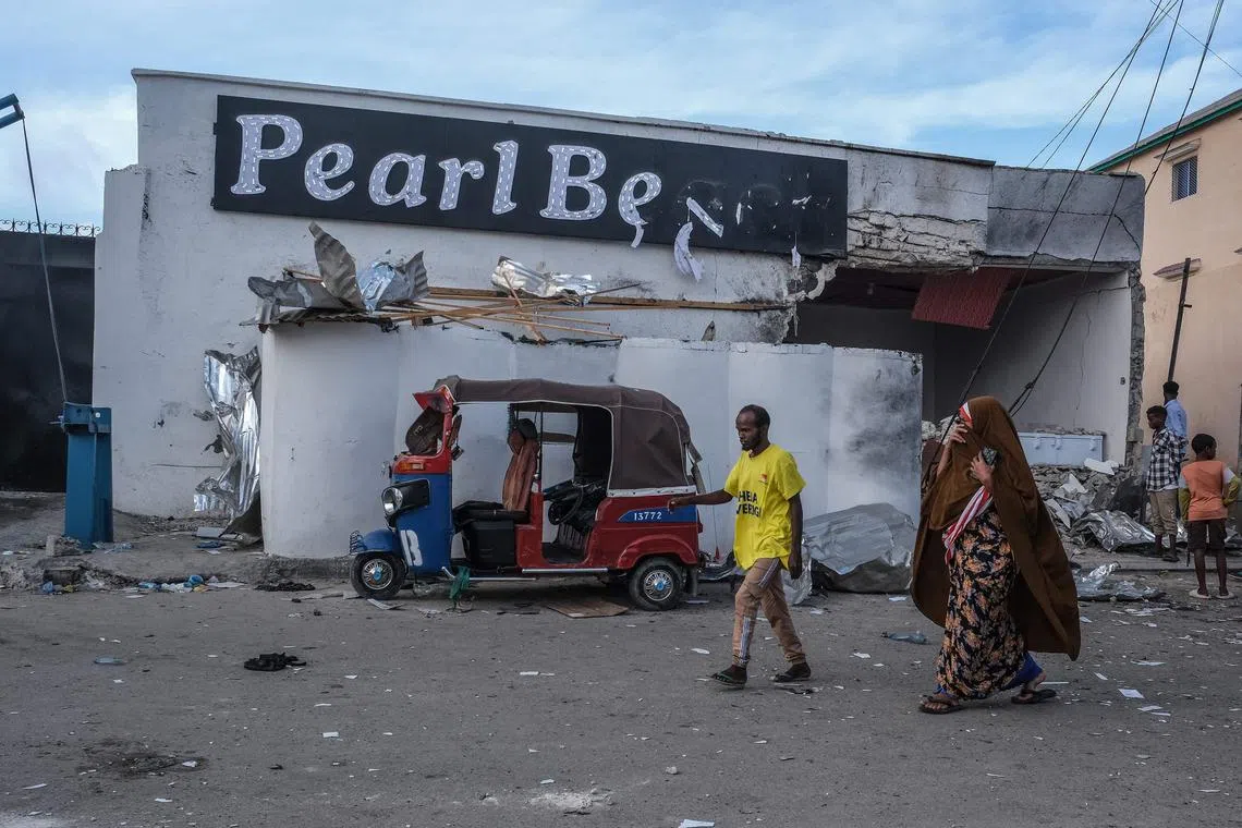 Residents walk past a damaged tuk-tuk left outside the site of an attack at the Palm Beach Hotel in Mogadishu.
