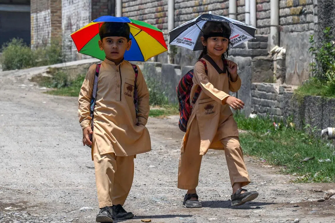 School children wearing umbrella hats to shelter from the sun, make their way to home along a street in Peshawar on June 19, 2023. (Photo by Abdul MAJEED / AFP)