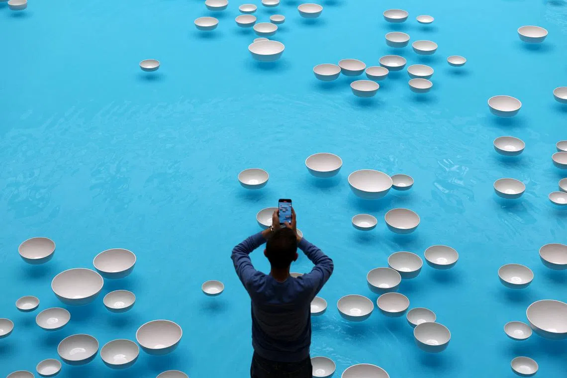 A visitor taking a picture of the artwork "clinamen", an aquatic and musical installation, by artist Celeste Boursier-Mougenot displayed at the Bourse de Commerce - Pinault Collection museum in Paris, France, on June 5, 2025.
