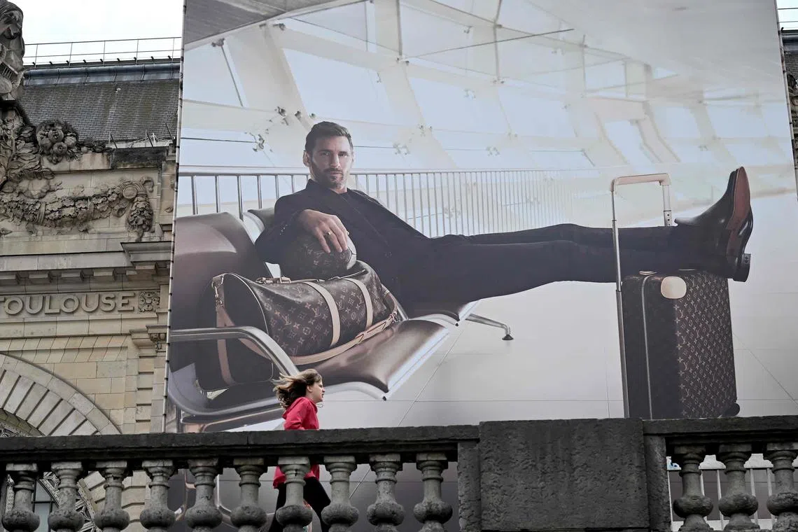 A hoarding of Lionel Messi posing with luggage made by the Louis Vuitton brand in Paris. The footballer did not come from much money but has earned a significant amount. 
