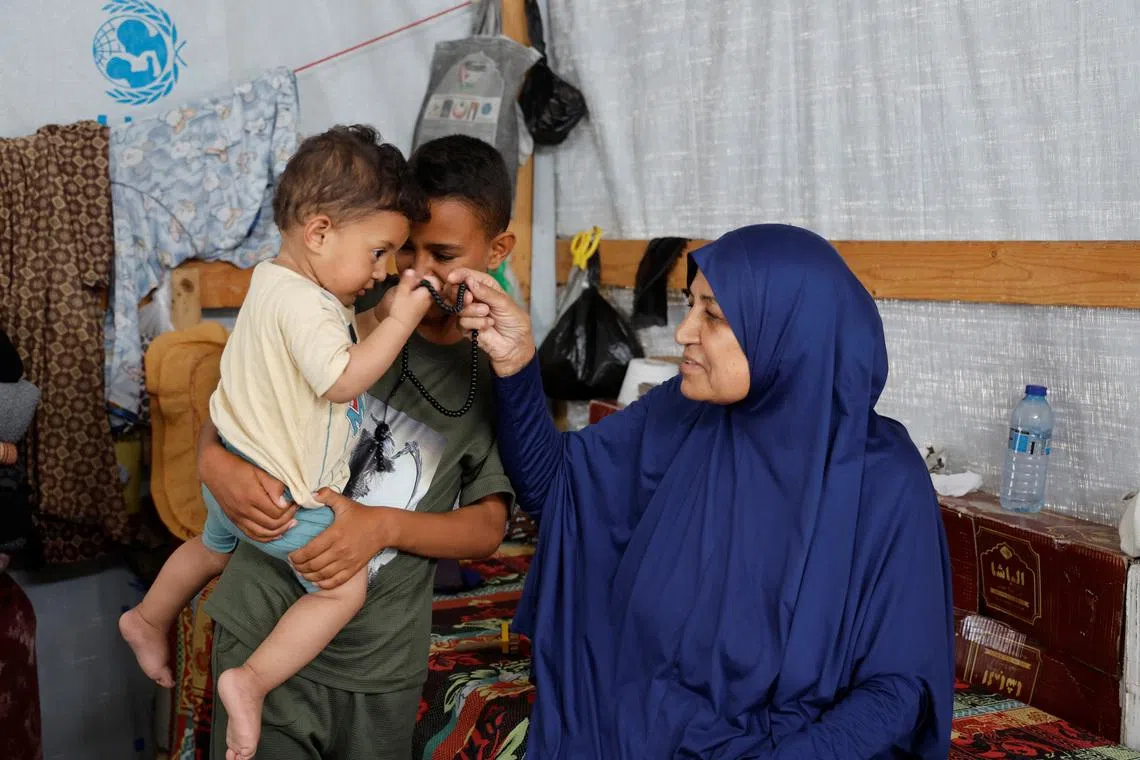 Palestinian Najia Abu Lehia sits with her grandchildren inside a tent at a camp for displaced people, as she speaks about her wish to perform hajj amid restrictions preventing Palestinians in Gaza from travelling to Saudi Arabia, in Khan Younis in the southern Gaza Strip, May 18, 2026. REUTERS/Haseeb Alwazeer