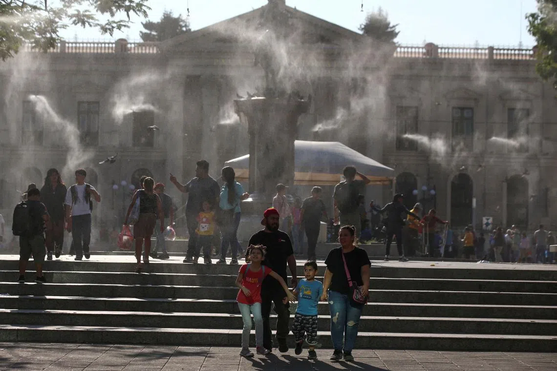 FILE PHOTO: People walk as water is sprayed by a system to alleviate the high temperatures caused by a heat wave, at the Gerardo Barrios square, in San Salvador, El Salvador, March 27, 2024. REUTERS/Jose Cabezas/File Photo