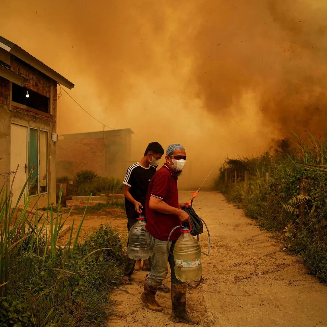 Residents carrying containers of water as a wildfire burns near a residential area in Banyuasin, South Sumatra province, Indonesia, on Oct 7.